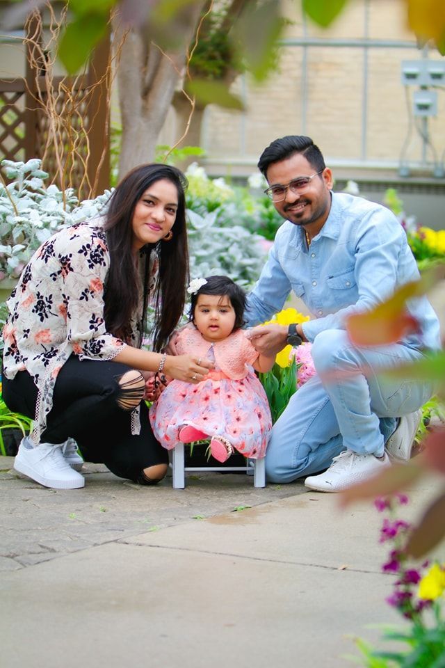 A man and woman are posing for a picture with a baby girl sitting on a stool.