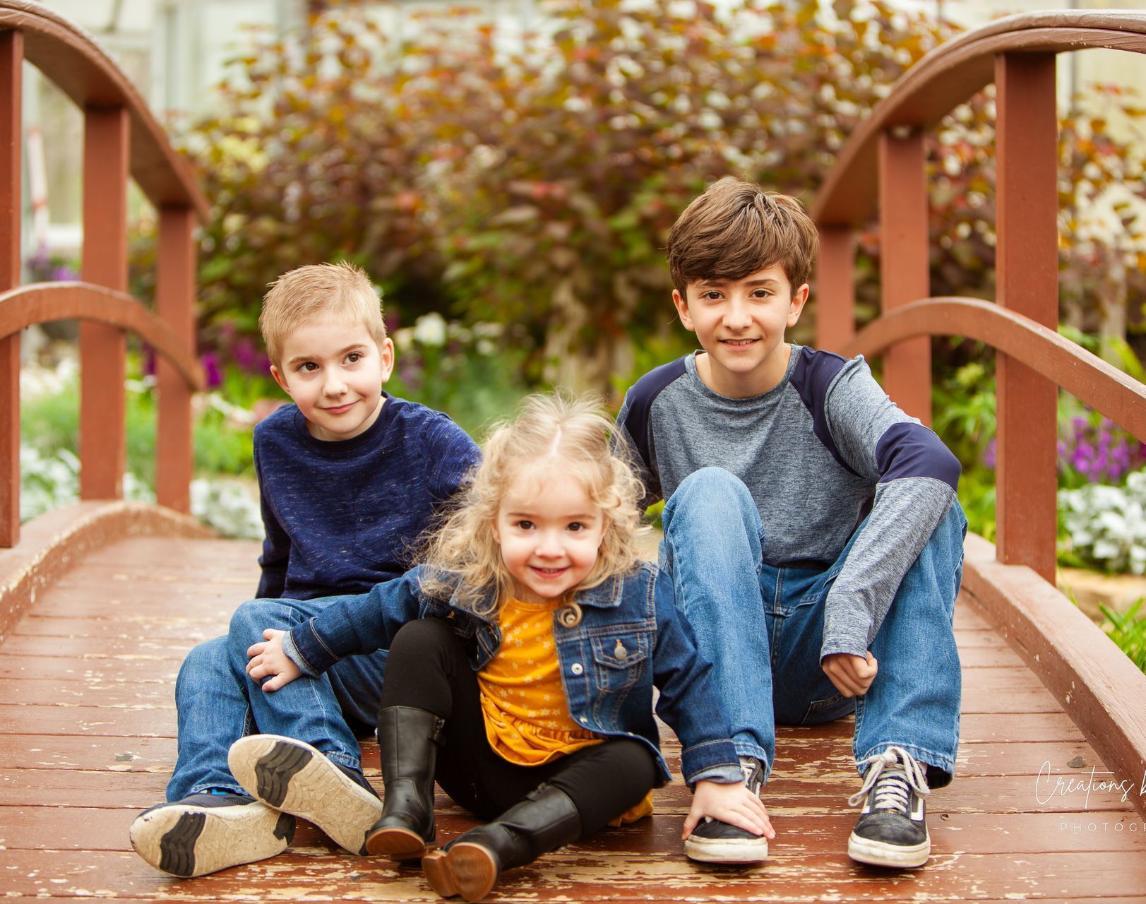 Three children are sitting on a wooden bridge.