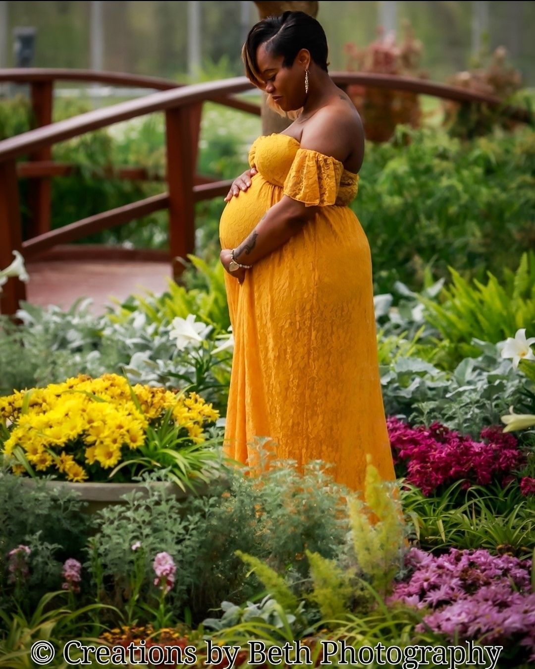 A pregnant woman in a yellow dress is standing in a garden
