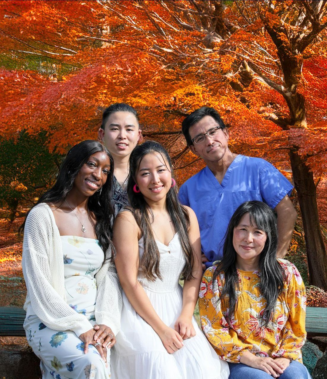 A group of six people smiling at the camera with vibrant red fall foliage in the background.