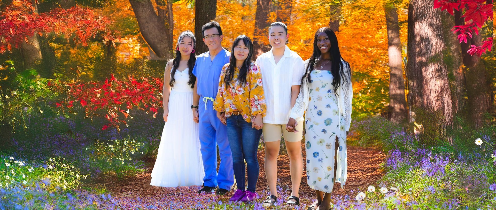 A group of five people posing in front of autumn foliage. They are standing on a flower bed with an array of colorful plants and trees.