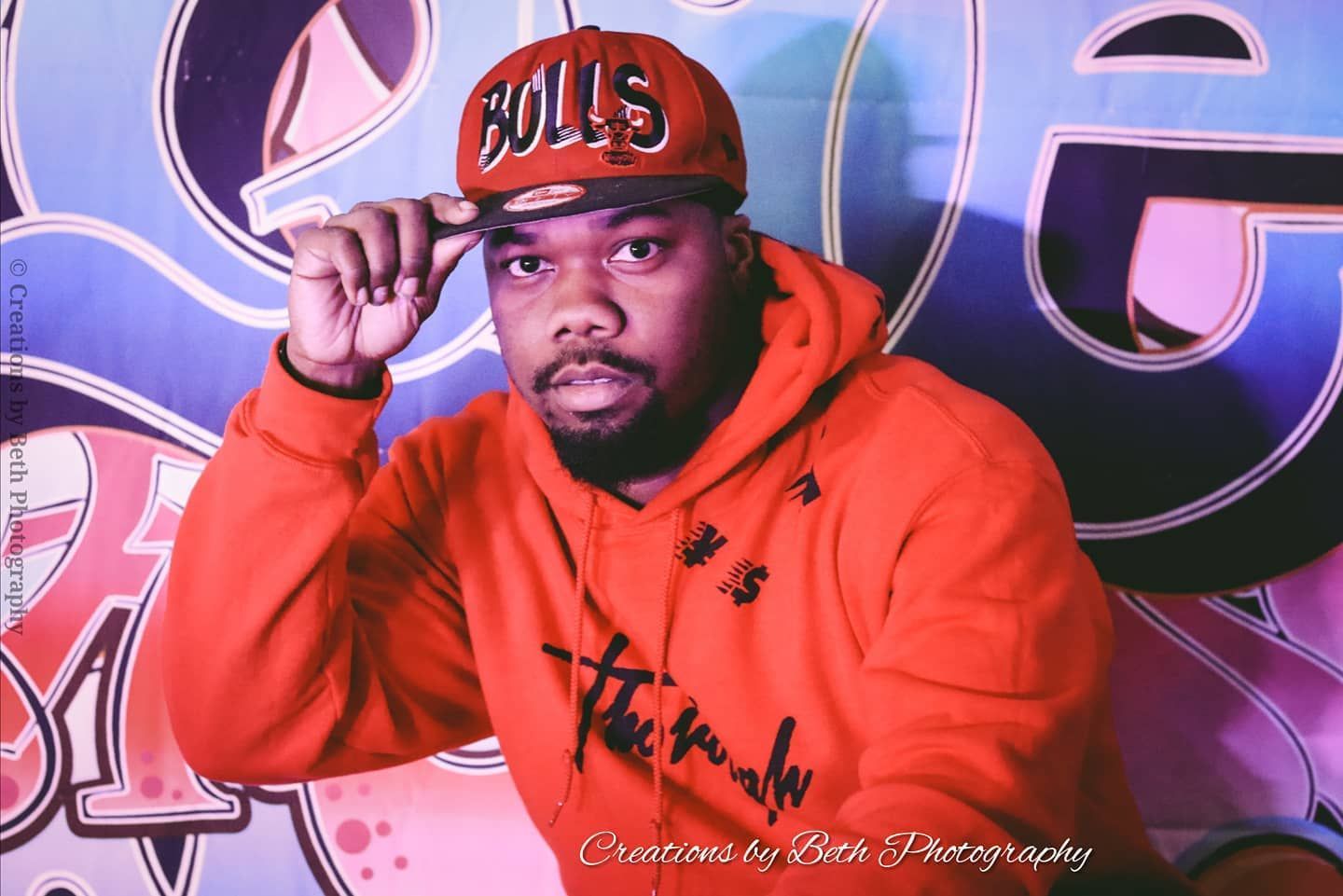 Man in red hoodie and Bulls cap, hand on cap. Graffiti background, studio shot.