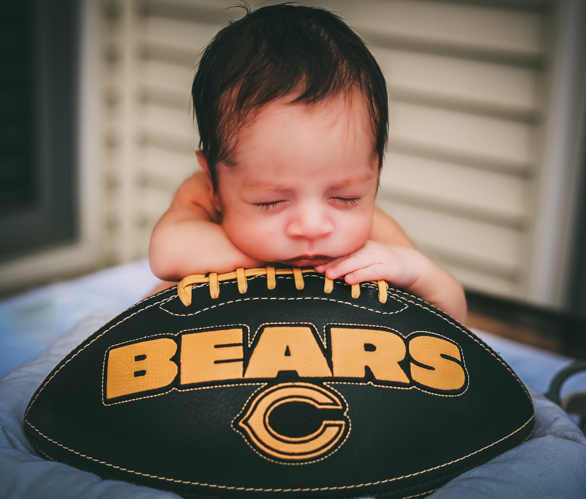 Sleeping baby resting on a Chicago Bears football, with a gold-and-black logo visible