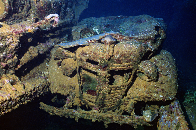 Underwater view of a car submerged in the ocean, covered in marine growth.