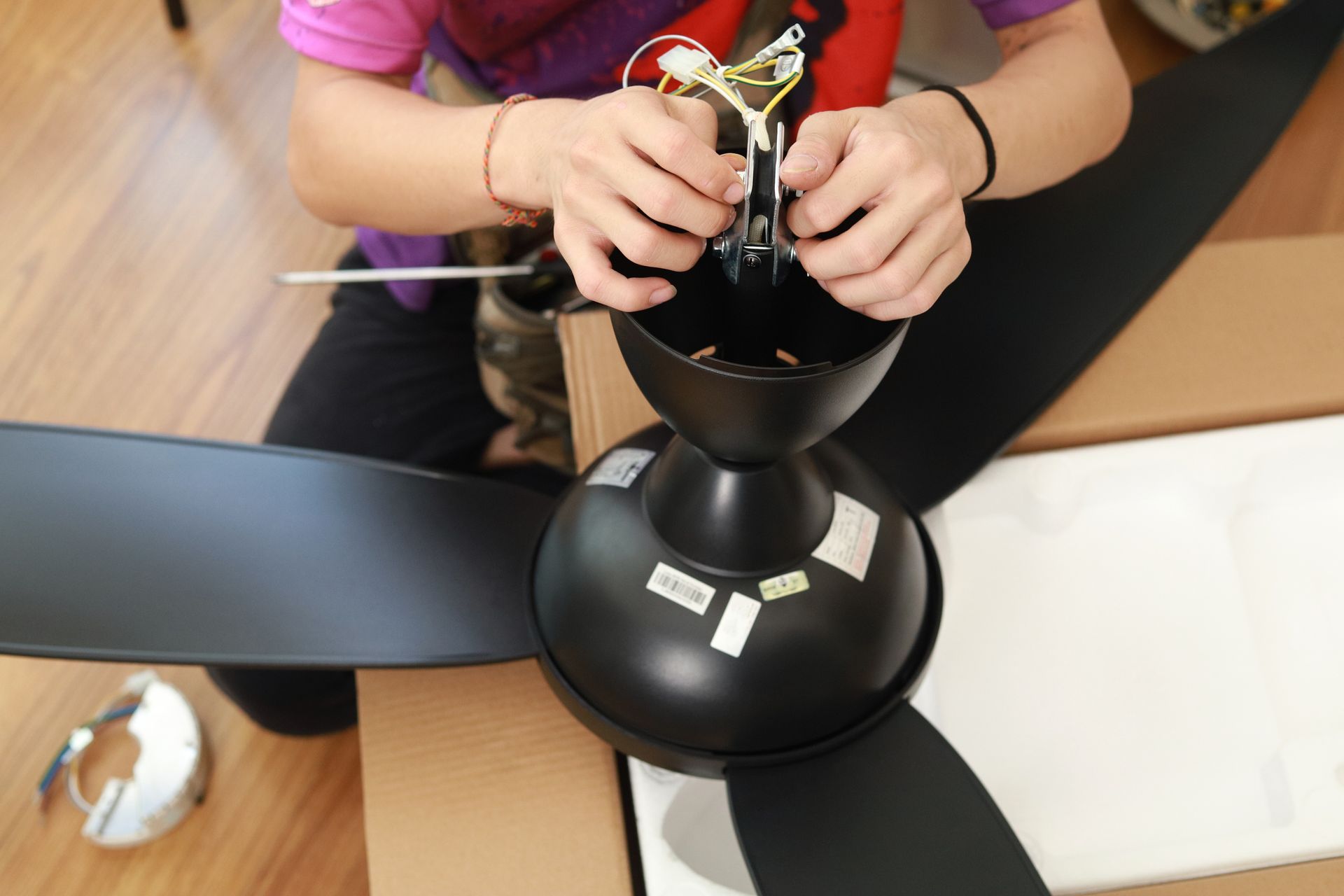 Person installing a black ceiling fan, connecting wires.