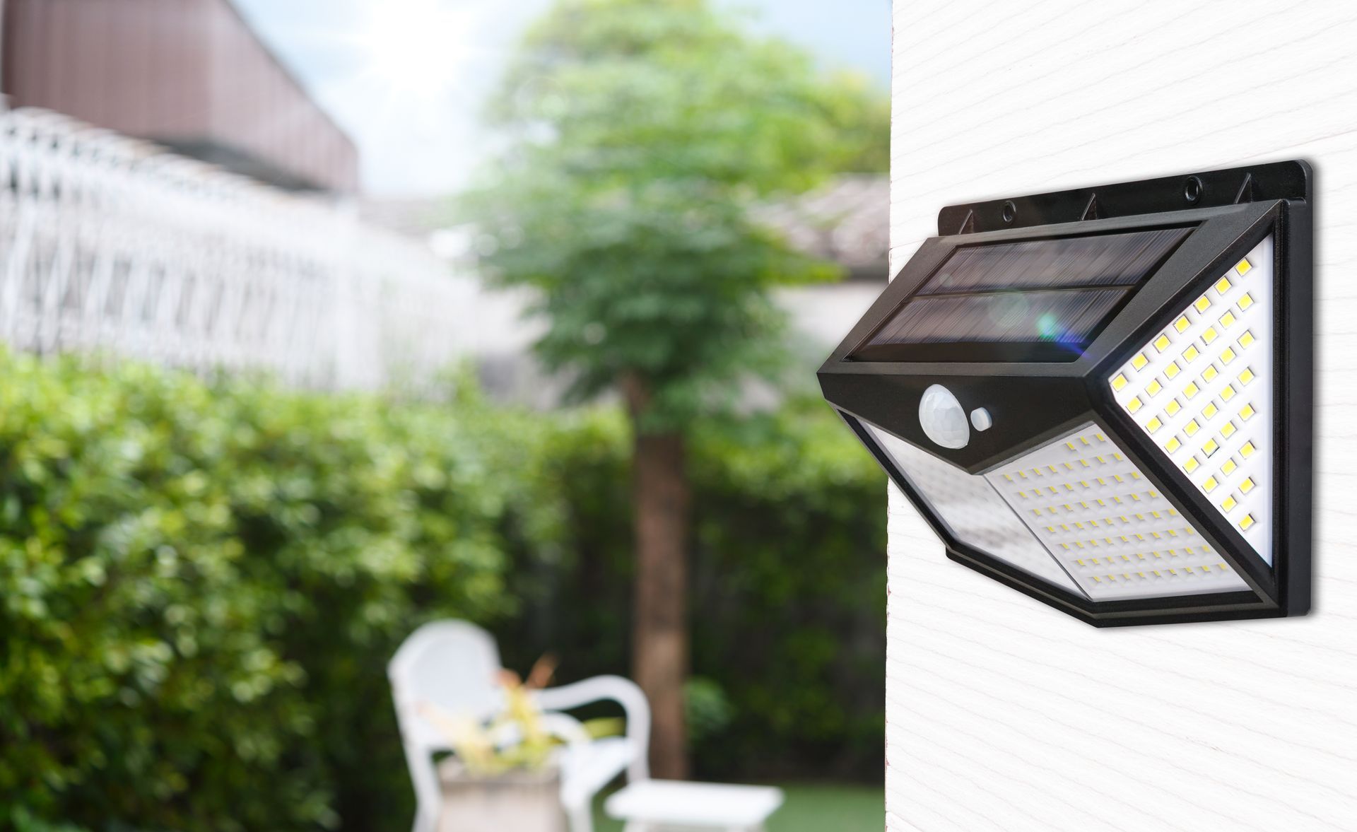 Black solar-powered security light with motion sensor mounted on a white wall in a yard.