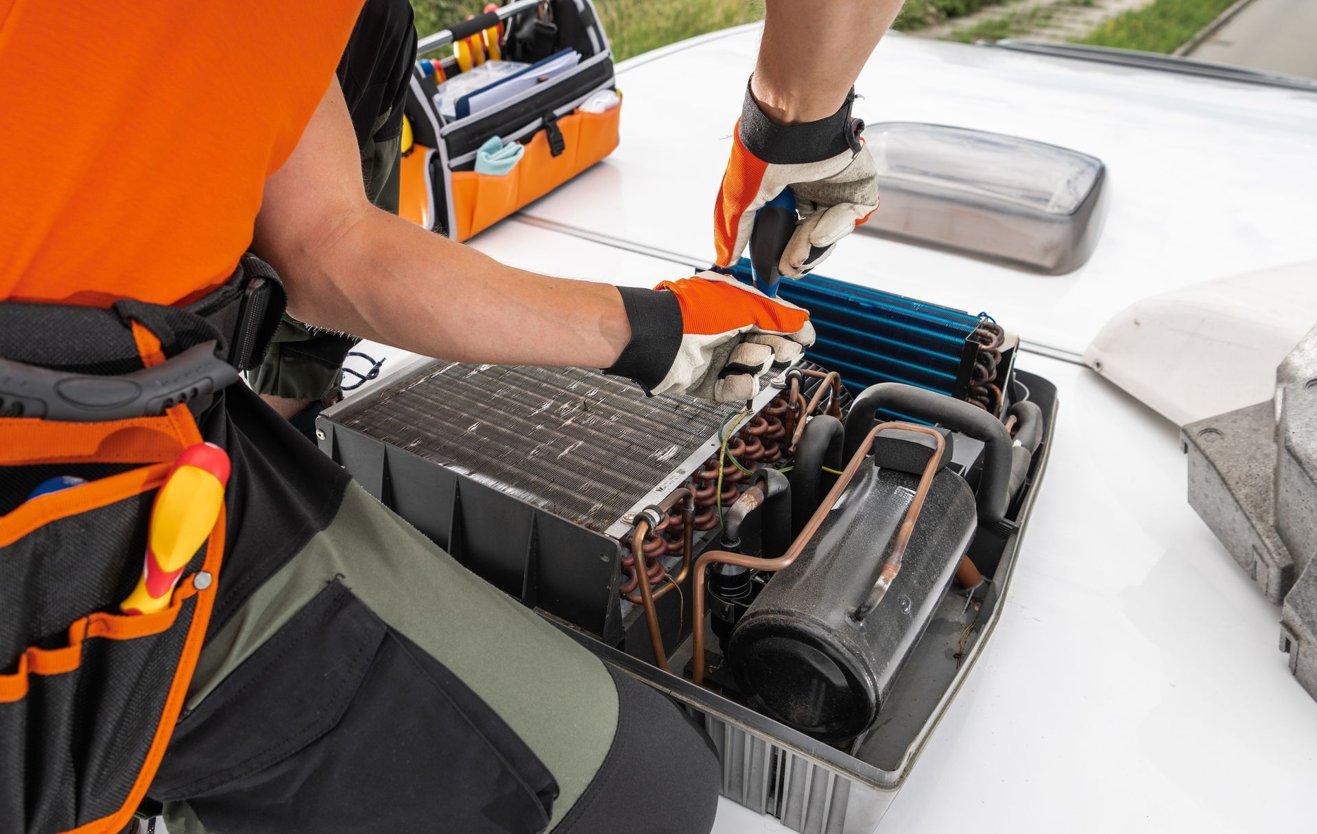 HVAC technician repairs an air conditioner on a rooftop. He wears gloves and uses tools.