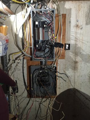Electrical panel with exposed wires mounted on a concrete wall.