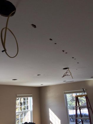 Ceiling with multiple recessed light holes, unfinished wiring, and a ladder by a window.