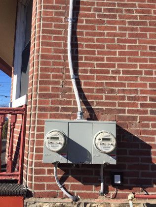 Gray electrical meter boxes mounted on a red brick wall with conduit running up the wall.