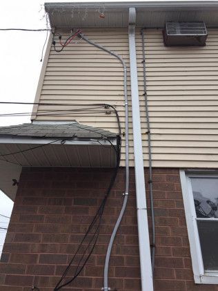 Exterior view of a two-story building with electrical wiring on the siding and along a downspout.