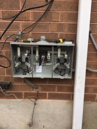 Metal electrical meter box on brick wall with exposed wiring.