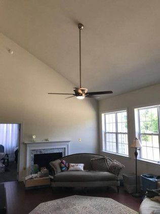 Living room with a high ceiling, couch, fireplace, windows, and a ceiling fan.