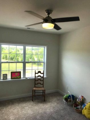 A room with a window, a chair, and a ceiling fan. Baskets of toys sit on the floor.