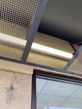 Overhead view of a building's exterior. Grid-covered metal frame and fluorescent lights above a window.