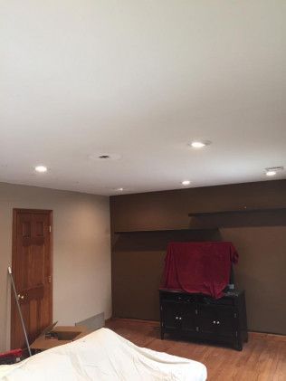 Bedroom with brown and tan walls, recessed lighting, wood door, and a dresser with a red cover.