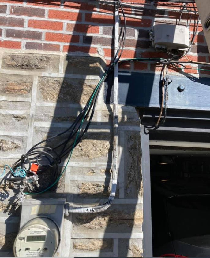 Exterior wall with electrical equipment, including wiring, meter, and box, attached to brick and stone.