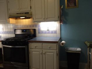 Kitchen with white cabinets, blue walls, a stainless steel stove, and a black trash can.