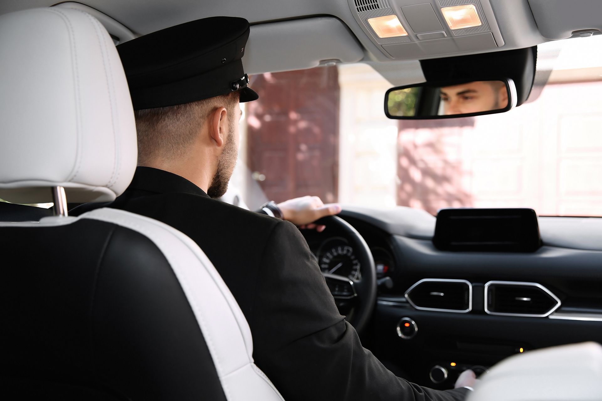 Chauffeur in a black uniform drives a car.