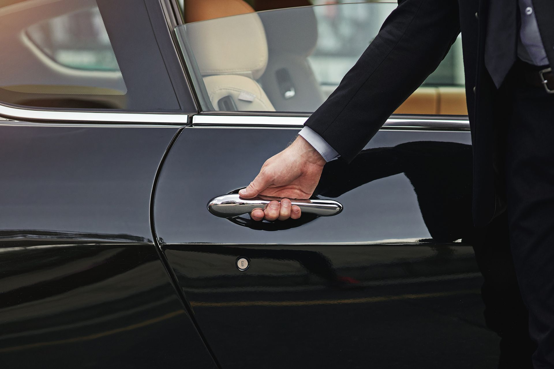 Person in a suit opens the door of a black car.