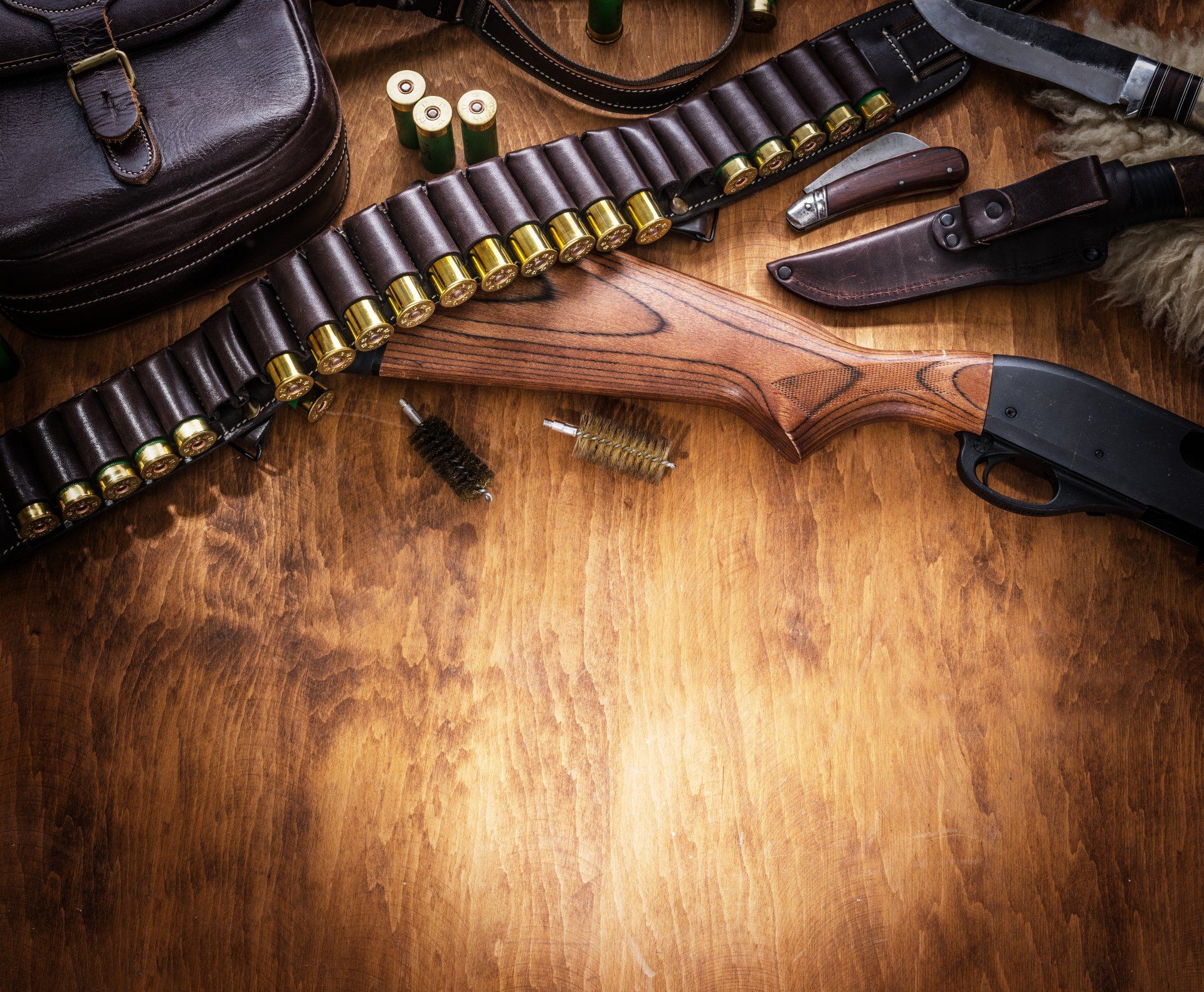 Hunting equipment - pump action shotgun, 12 mm hunting cartridge and hunting knife on the wooden table.