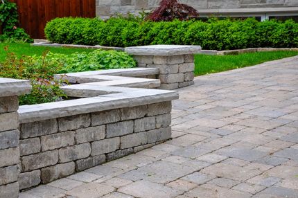 Stone walkway and retaining wall with green lawn and bushes in a landscaped yard.