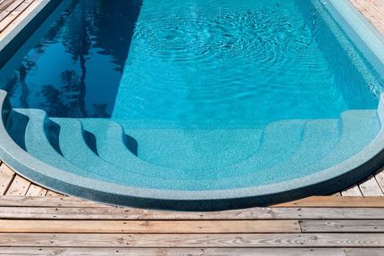 Pool with blue water and steps, surrounded by wooden decking, reflecting sunlight.