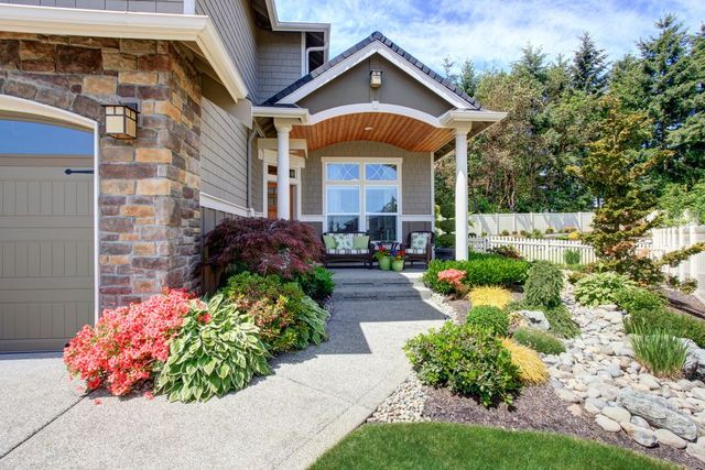 House exterior with stone facade, covered porch, and landscaped garden with various colorful plants.
