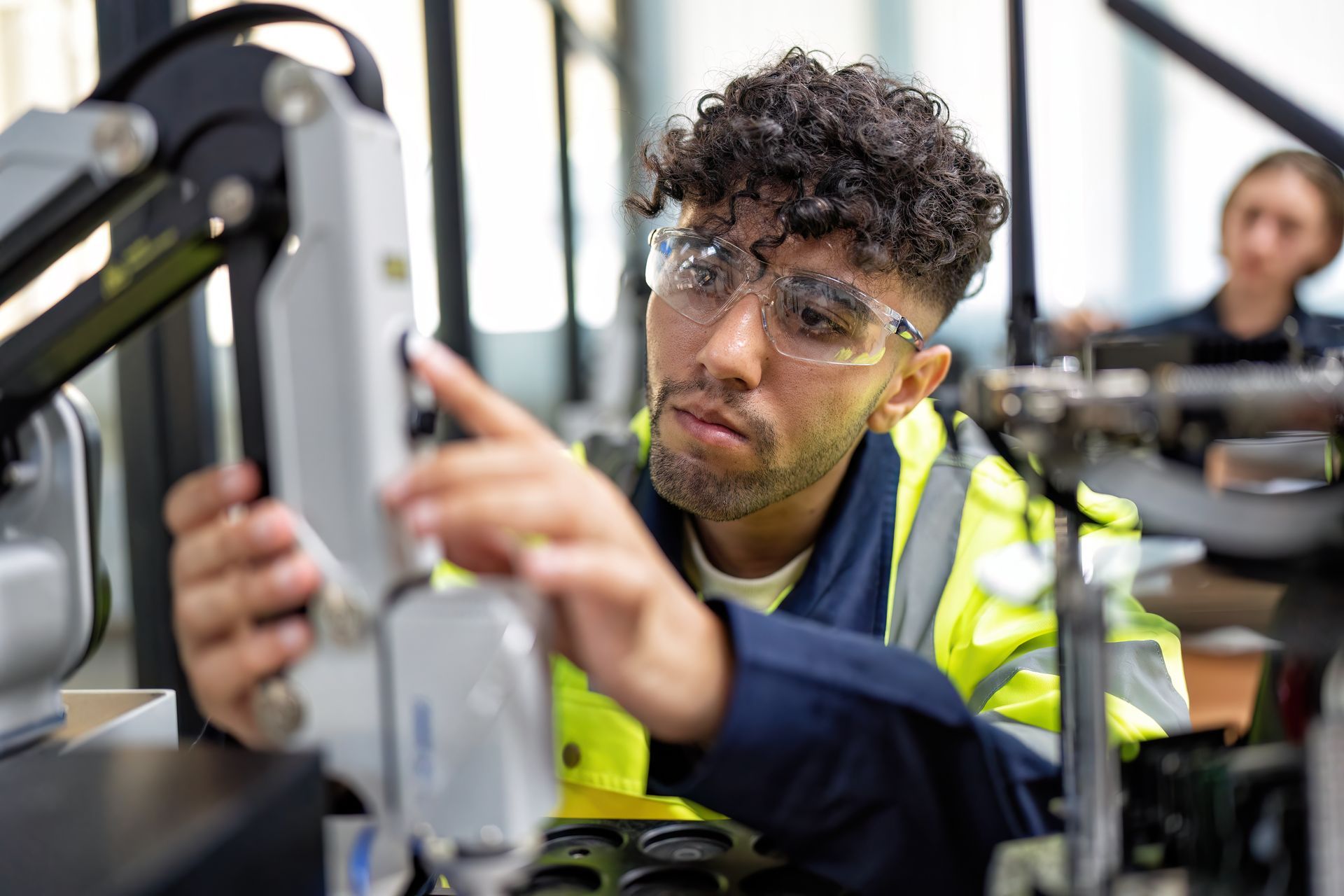 Man in safety glasses adjusts robotics arm in a workshop setting.