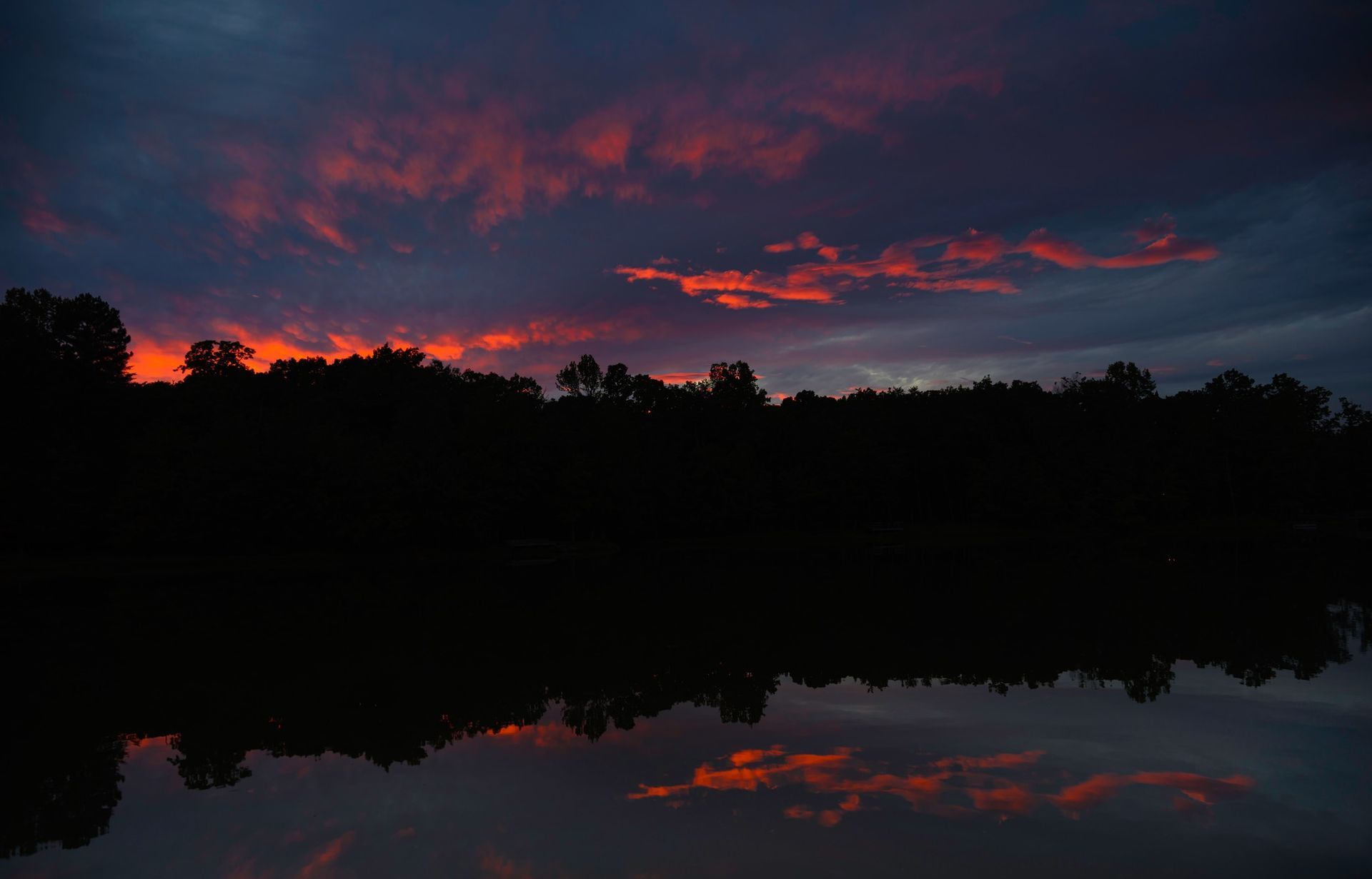 A sunset over a lake with trees in the foreground and a reflection of the sky in the water.