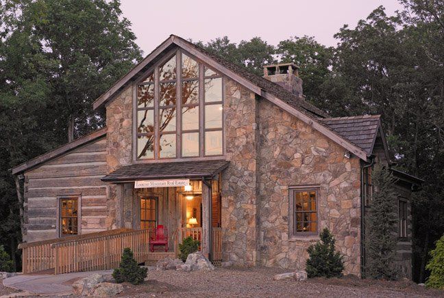 A large stone house with a lot of windows is surrounded by trees.