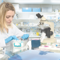 A woman in a lab coat and blue gloves is working in front of a microscope.