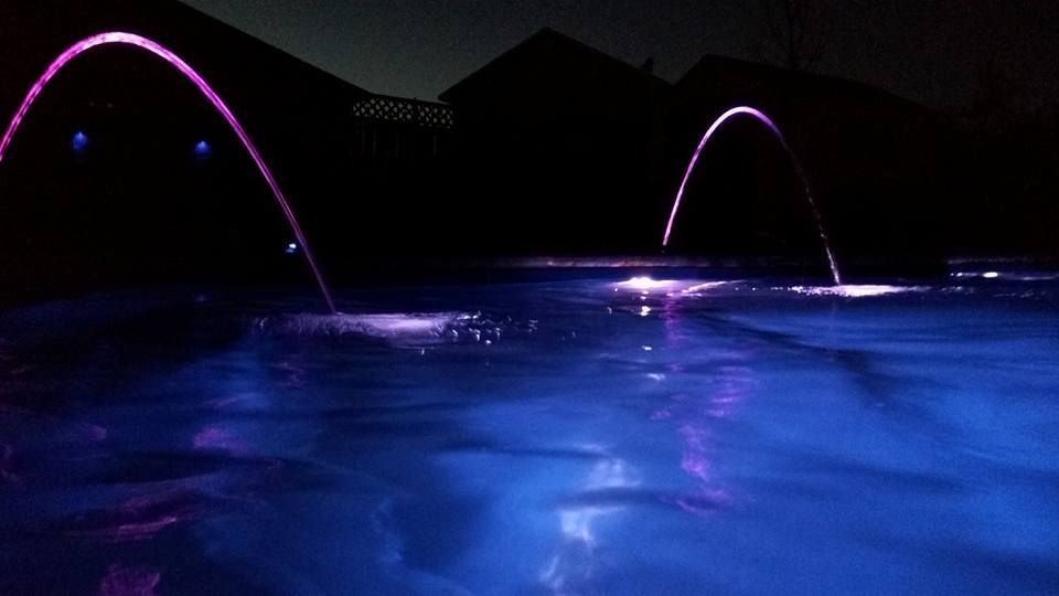 A swimming pool is lit up at night with purple lights.