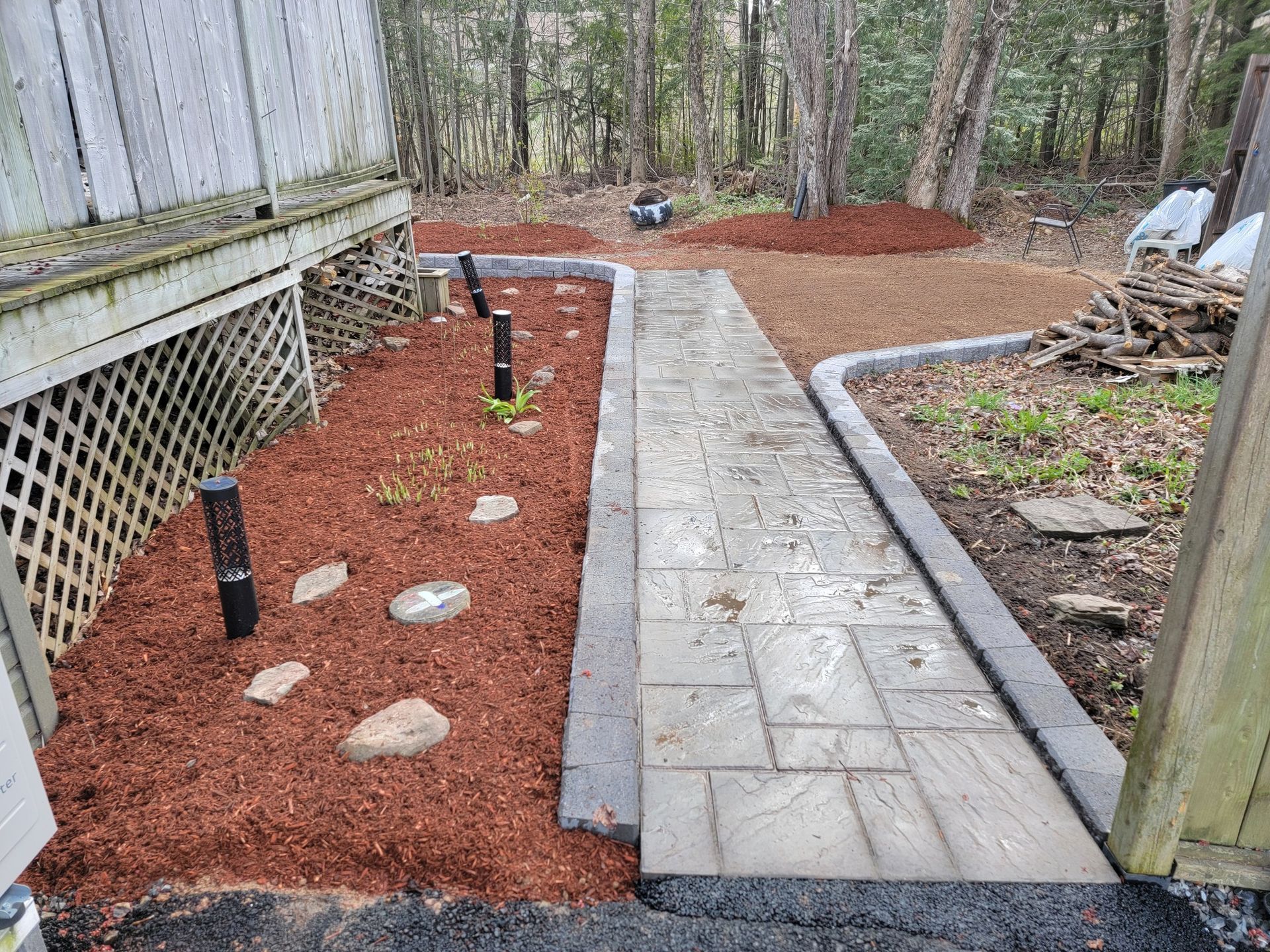A walkway leading to a backyard filled with mulch and trees.
