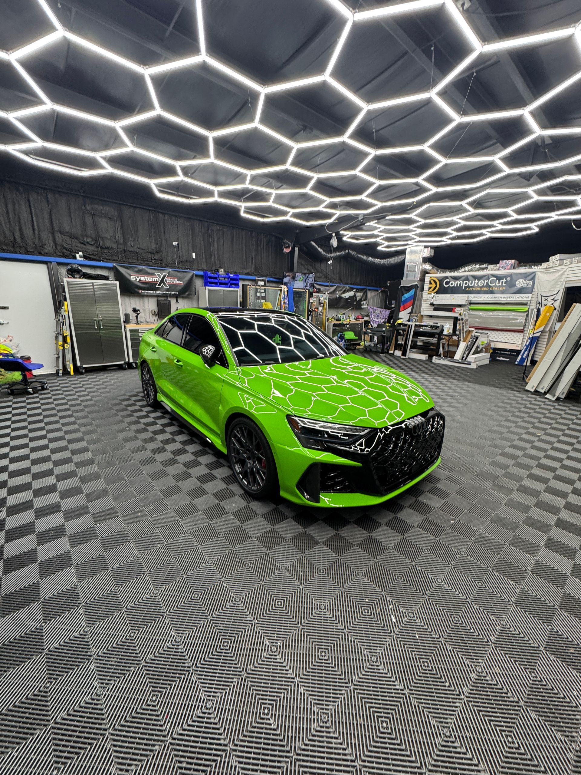 Green sports car in a garage with honeycomb ceiling lights.