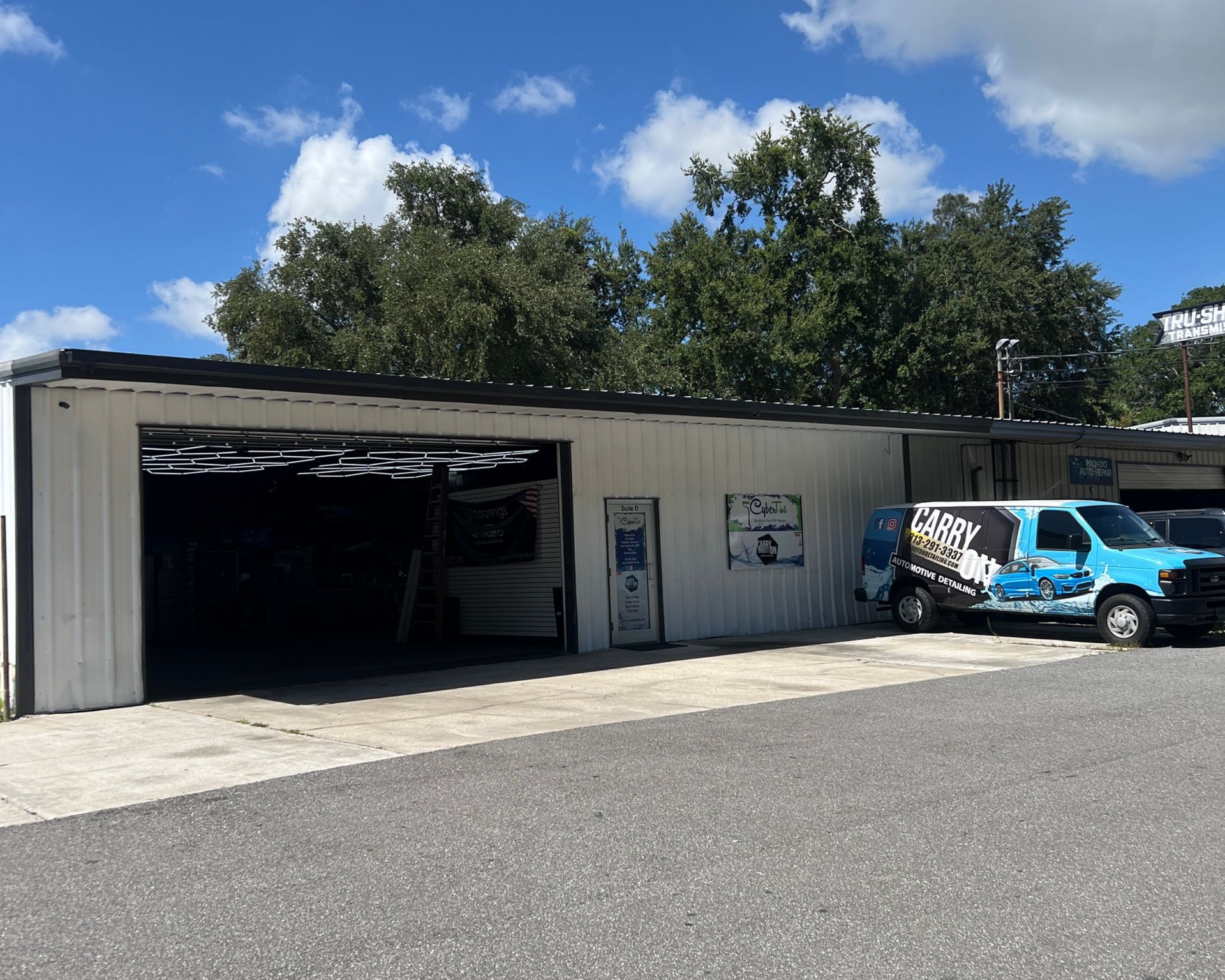 White commercial building with open bay door, blue van parked in front. Cloudy sky.