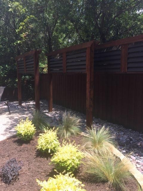 Dark stained wooden fence with open-slatted top sections. Landscaping features green and yellow bushes and grasses.