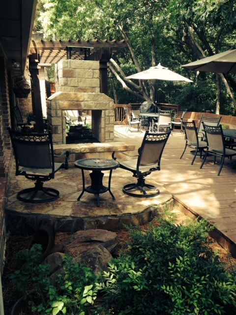Outdoor patio with fireplace, seating, umbrellas, and surrounding trees.