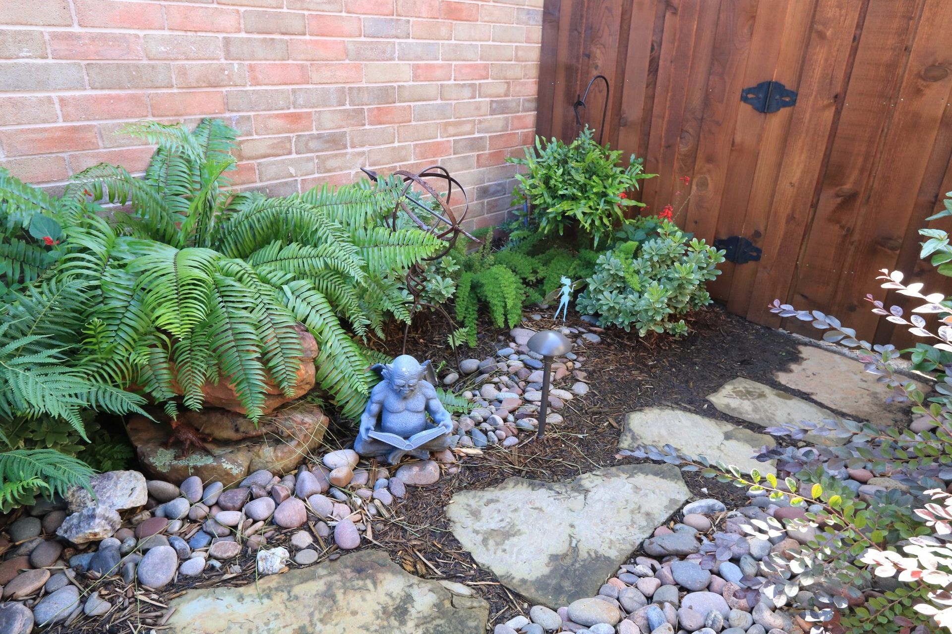 Zen garden with ferns, a statue, and stepping stones.