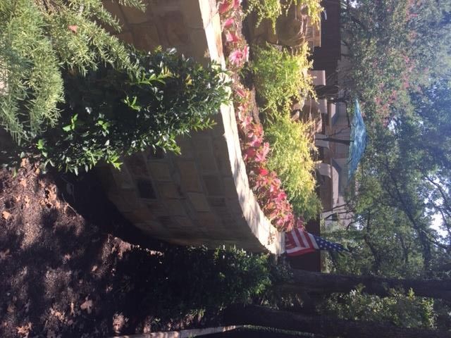 Stone wall planter overflowing with pink and yellow flowers, American flag nearby.