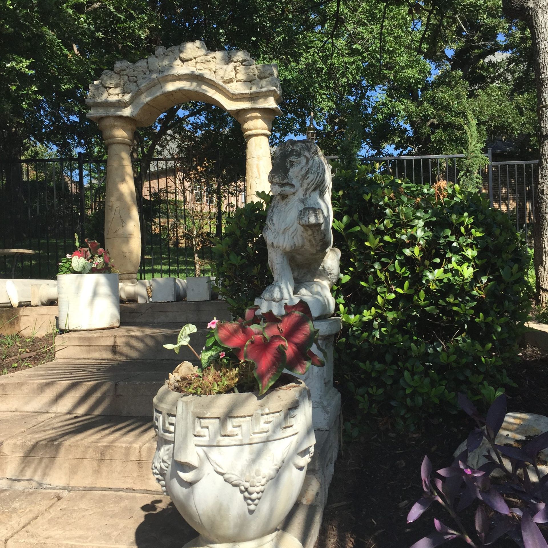 Stone archway and lion statue in a garden, with a potted plant in the foreground.