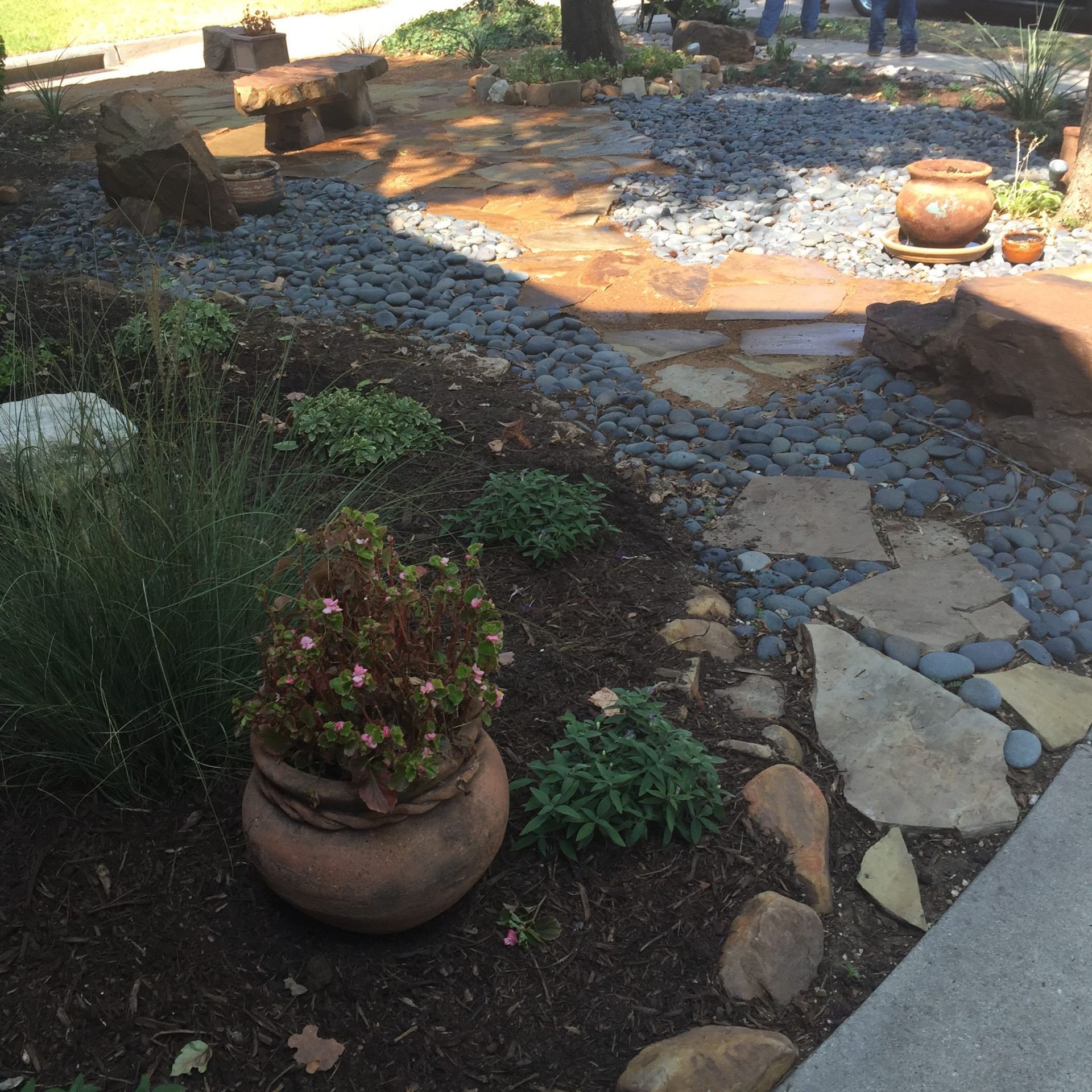 Stone path and flower beds with rocks and a bench in a garden setting.