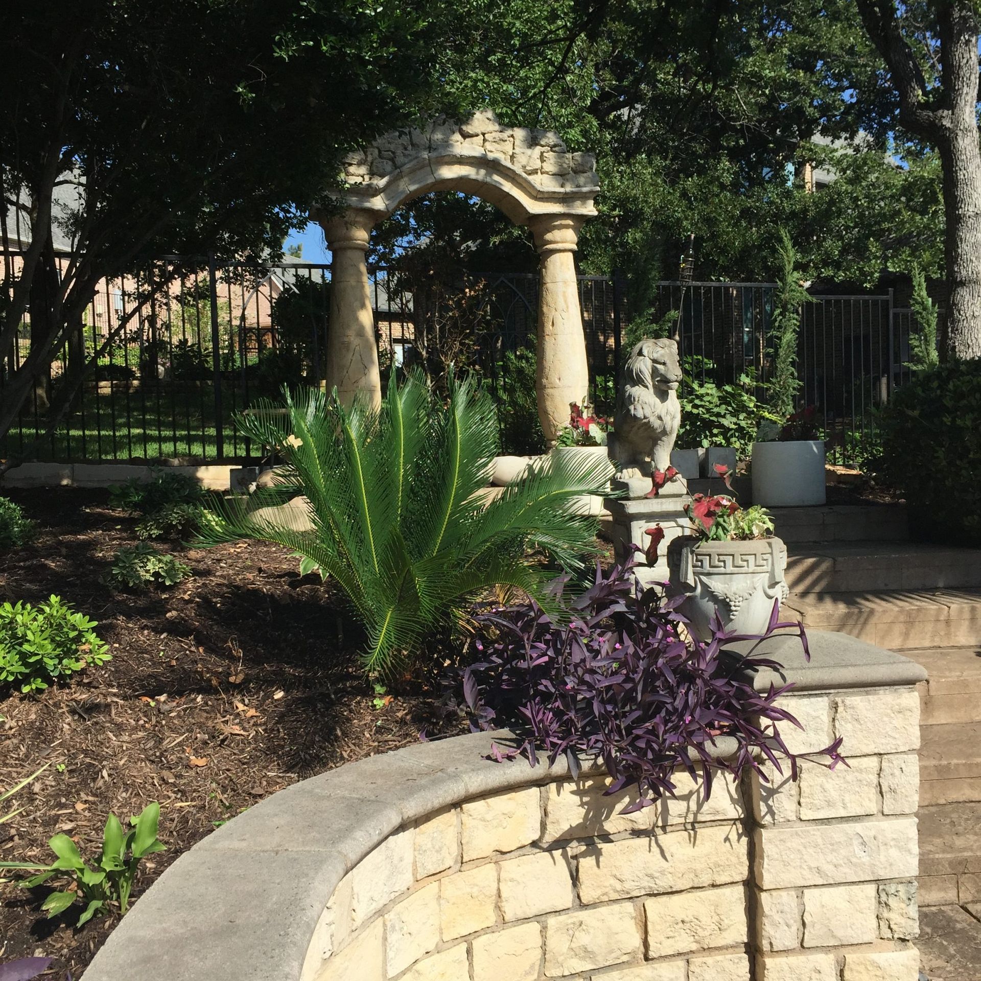 A decorative garden with stone archway, ornate fountain, and colorful plants.