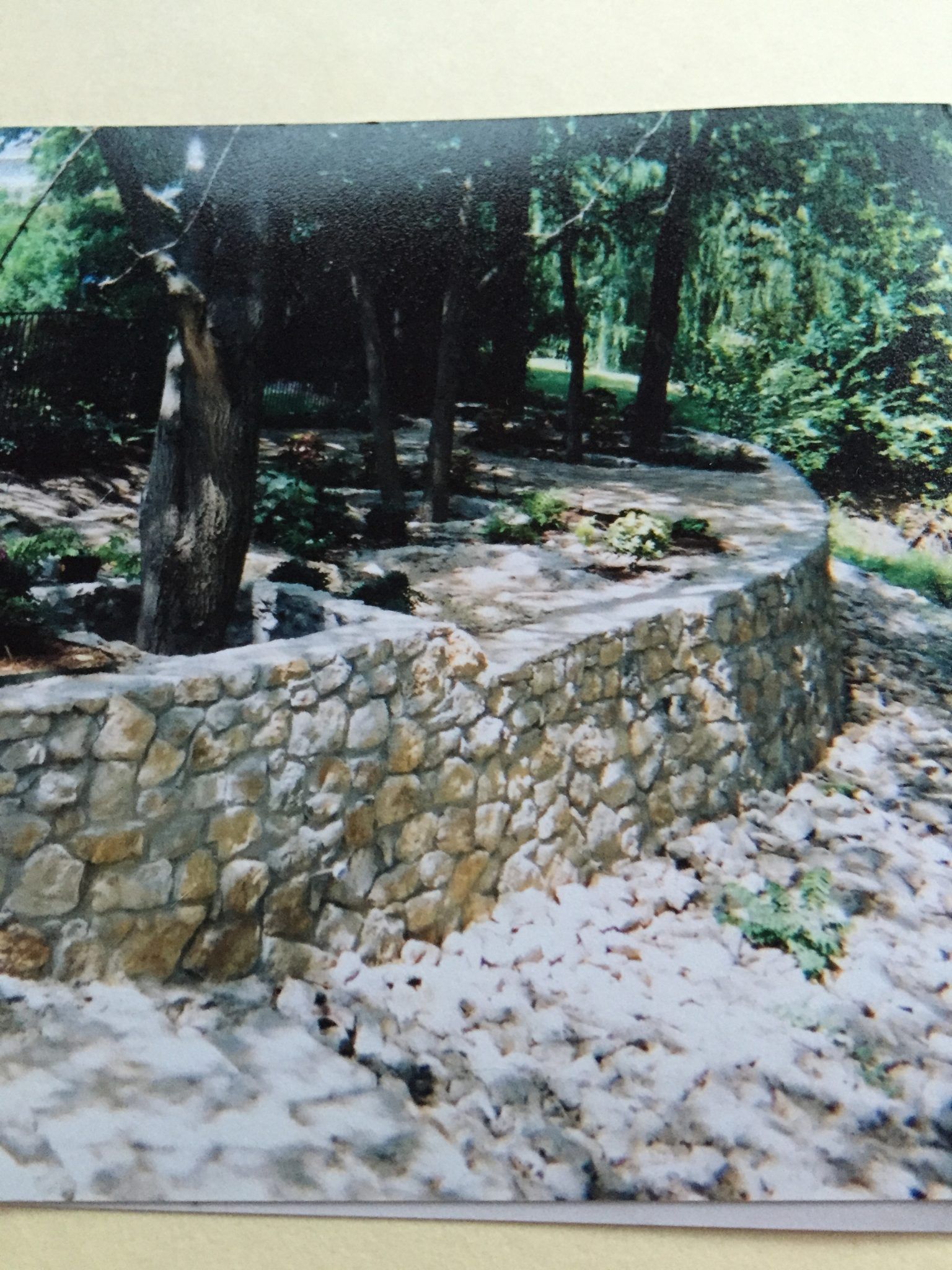Stone retaining wall curves through a wooded area.