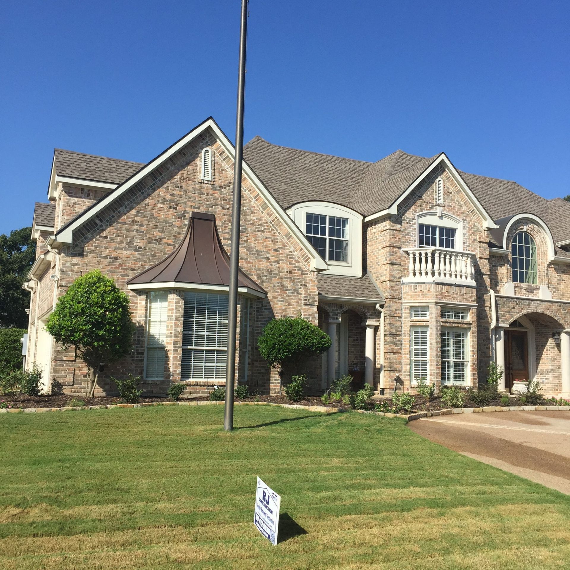 Two-story brick house with a manicured lawn under a blue sky. A flagpole stands in front.