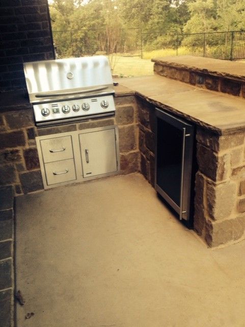 Outdoor kitchen with stainless steel grill, cabinets, and a refrigerator built into stone counters.