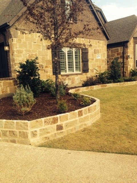 Stone house with a landscaped front yard featuring a curved retaining wall and greenery.