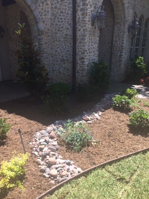 Landscaped yard with a dry creek bed, mulch, plants, and a stone facade.