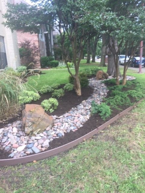 Landscaped garden bed with rock path, trees, and plants along building's lawn.