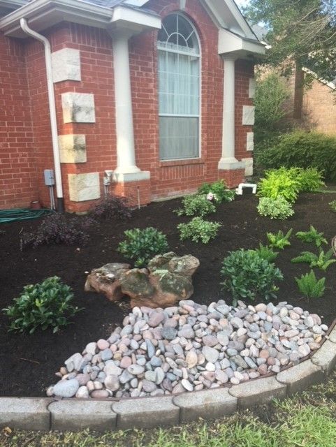 Red brick house with landscaped garden, featuring dark mulch, river rocks, and various green plants.